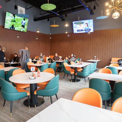 Interior with wood slat walls, tables, orange and teil chairs, and TVs.