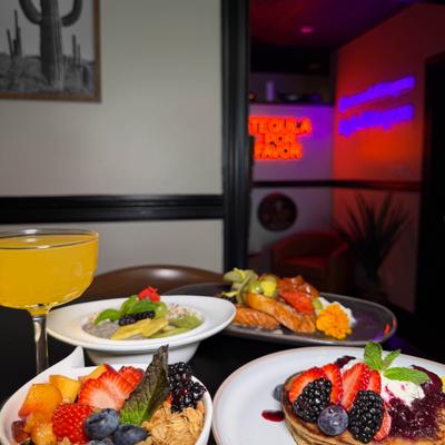 Colorful brunch spread featuring berry pancakes, fresh fruit, and a bright cocktail.