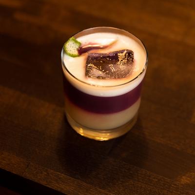 Layered cocktail with purple and cream tones garnished with citrus peel.