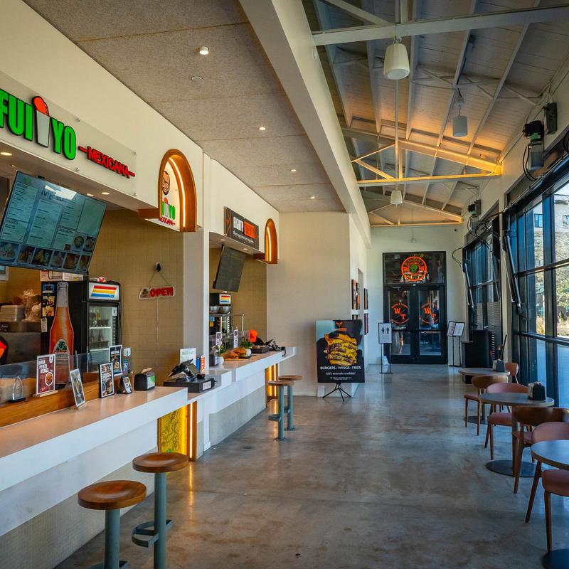 Casual dining interior with multiple food counters, menu screens, and seating near large windows