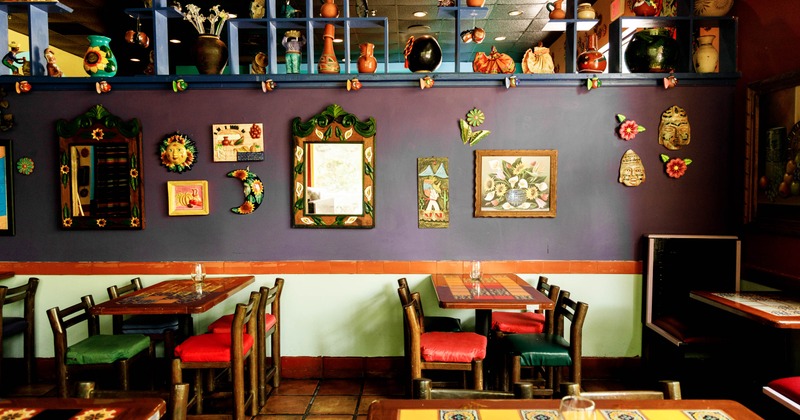 Interior with decorated walls, blue shelves displaying pottery, and wooden furniture with colorful cushions