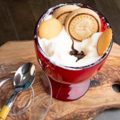 A tall red dessert glass filled with whipped cream, chocolate syrup and cookies..