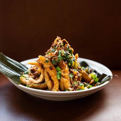 Crispy-fried fish served on a banana leaf with fresh herbs and scallions.