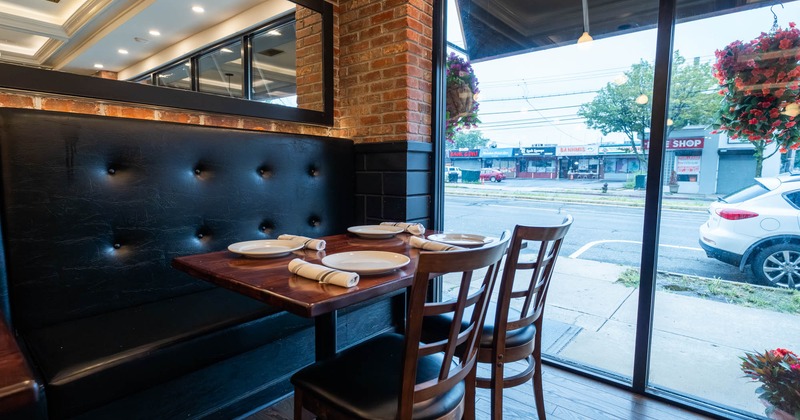 Interior, restaurant booth with a set table for four next to floor-to-ceiling windows overlooking the street