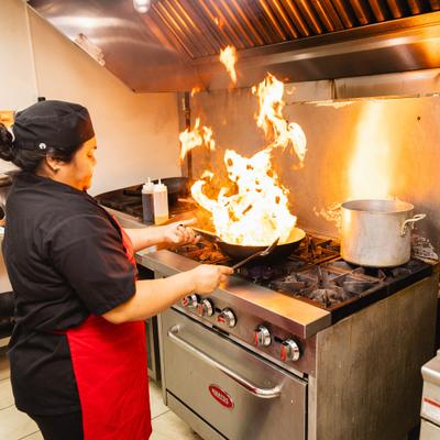 Chef cooking food over open flames on a stove.