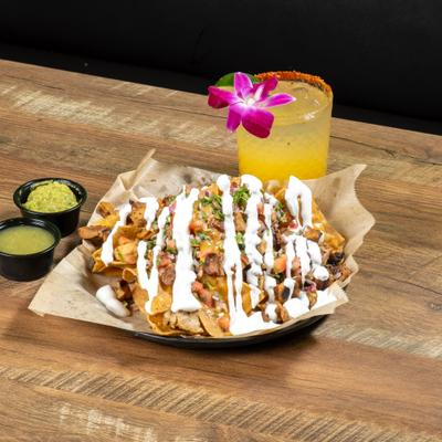 Carne Asada Nachos with salsa on the side and a glass of margarita with orchid garnish.