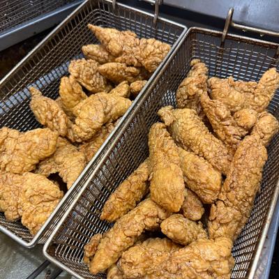 Fried chicken tenders fill two metal baskets in a fryer.