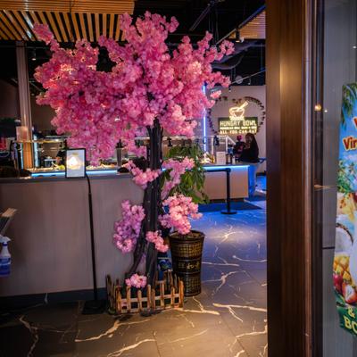Artificial pink cherry blossom tree placed near a dark wood restaurant entryway.