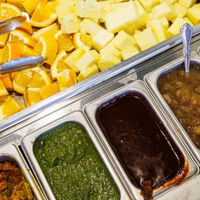 Indian food buffet featuring sliced oranges, cubed pineapples, and chutneys.