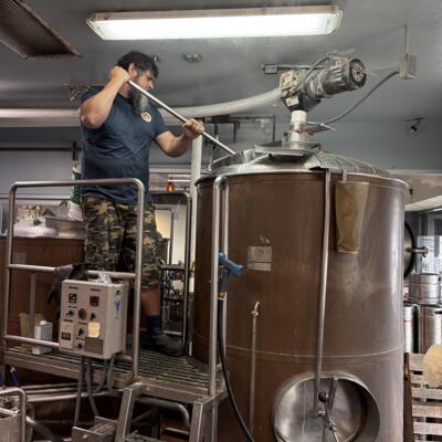 Brewmaster on step stiring grain in copper mash tank.