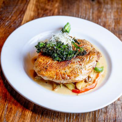 Plated roasted chicken breast sits on vegetables topped with broccoli and grated cheese.