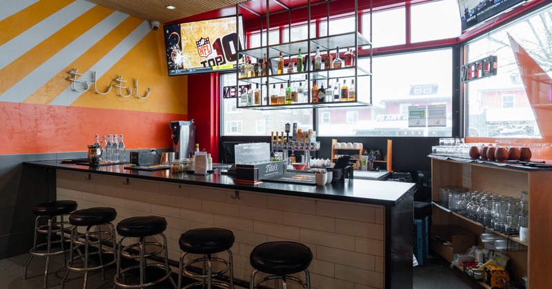Interior, bar area, bar stools, large window area, hanging shelves with liquor bottles