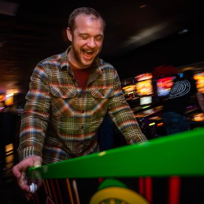 A guest joyfully plays pinball in a dimly lit arcade space.