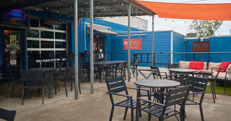Exterior with round tables and black chairs: sofa with cushions in the background
