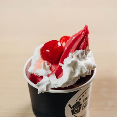 Pomegranate frozen yogurt topped with whipped cream and a cherry.