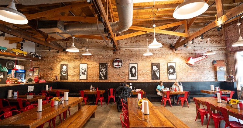 Interior of a rustic restaurant with brick walls, red chairs, and large wooden tables