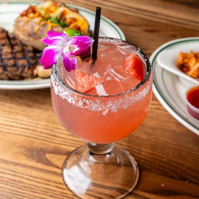 Watermelon margarita with orchid garnish in a stemmed, salt-rimed glass.