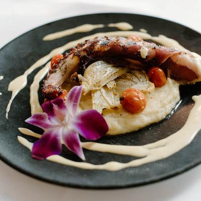 Grilled octopus and grits on a plate decorated with sauce and an edible flower.