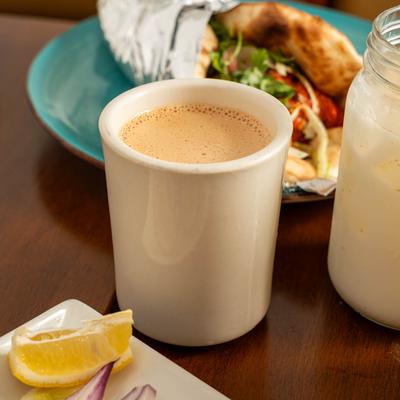 Close up of a mug of Chai on a table with food.