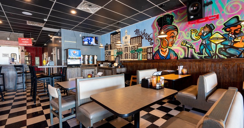 Interior, seating booths with tables, murals on the right wall, serving station in the back