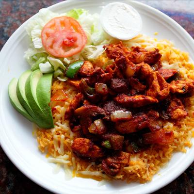 Grilled chicken pieces cooked with spices, served over rice with fresh veggies on the side.