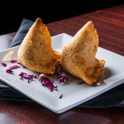 Two vegetable samosas on a white plate with cabbage garnish.