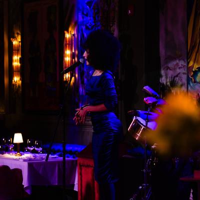 Singer holding the microphone during live music, artwork behind her.