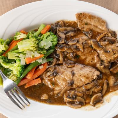 Chicken Marsala topped with mushroom sauce and served alongside vegetables.