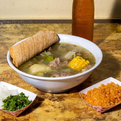 Chicken soup served with tortillas, rice, cilantro and onion, and a bottled soft drink.