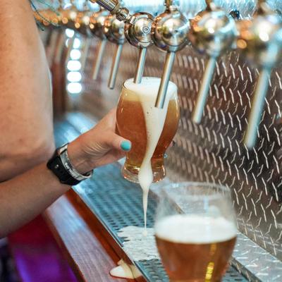 A person pours beer from a tap, overflowing the glass with foam.