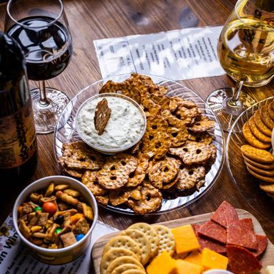 Pretzel chips and spinach dip, surrounded by wine glasses and a charcuterie board.