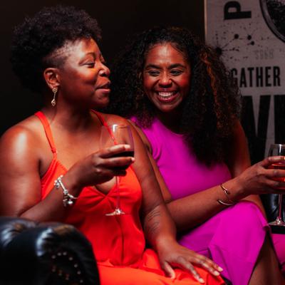 Two people smiling and holding glasses of wine in a bar setting.