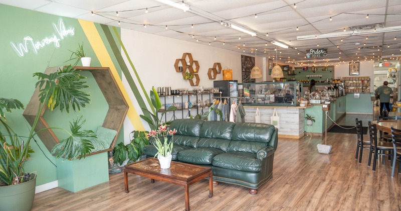 Interior of a cozy coffee shop with a green sofa, wooden elements, plants, and string lights