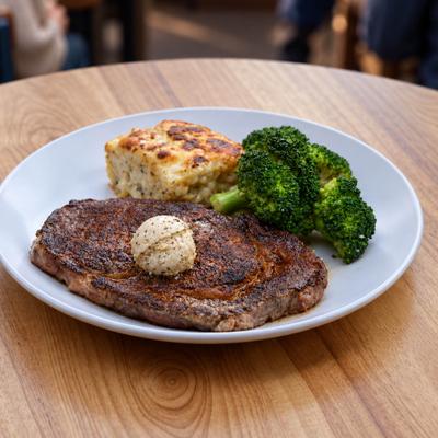 Ribeye steak topped with melting butter, served with gratin, and broccoli.