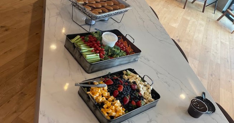 Buffet spread with fresh fruit, vegetable platter with dip, and sliders on a marble counter