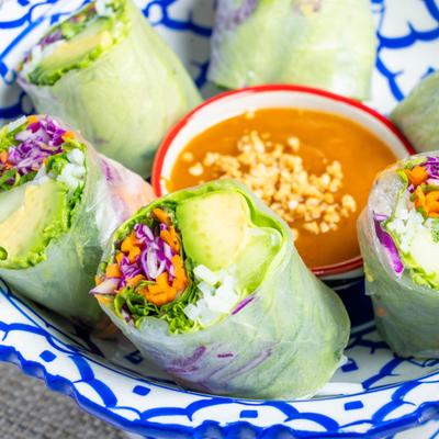 Fresh avocado summer rolls served with a cup of peanut sauce.