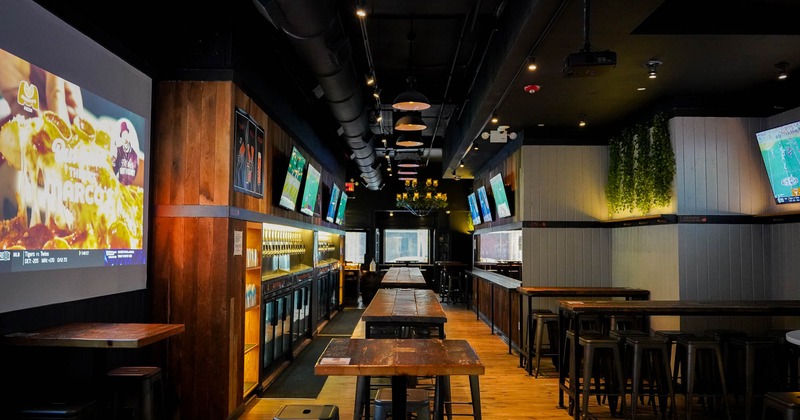 Interior of a bar with wooden tables, stools, TV screens