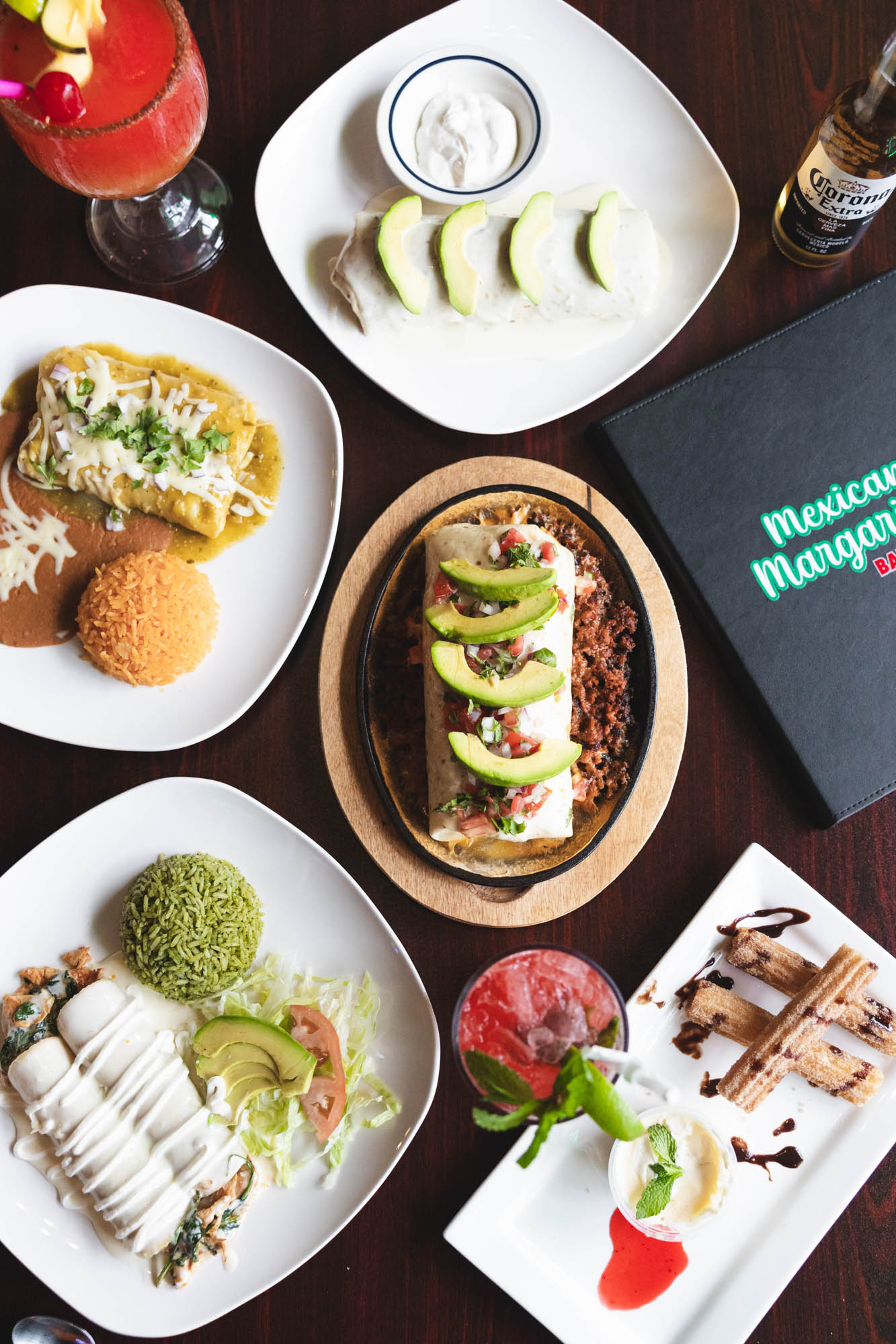 A spread of Mexican dishes and drinks including a burritos, enchiladas, churros, and margaritas