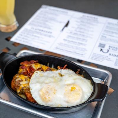 Fried eggs top cheese and bacon tater tots served in a black skillet.