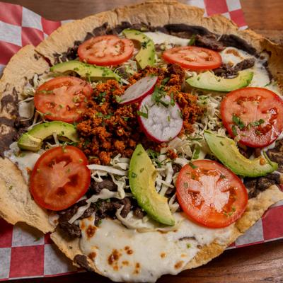 Tlayuda featuring crispy toasted tortilla covered in steak, chorizo, bean paste, avocado and tomato.