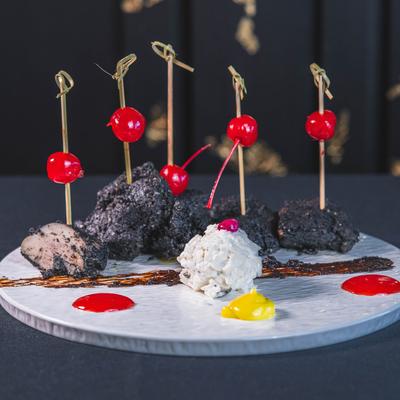 Decorative food arrangement with skewered cherries and dark coated items on a white plate.