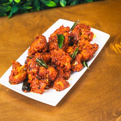 Crispy red fried chicken bites topped with curry leaves on a white plate.
