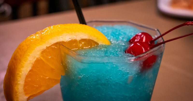 Blue-hued frozen cocktail garnished with an orange slice and cherries