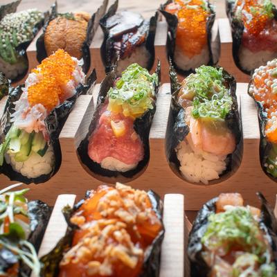 Assorted hand-rolled sushi with colorful toppings arranged in a wooden holder.