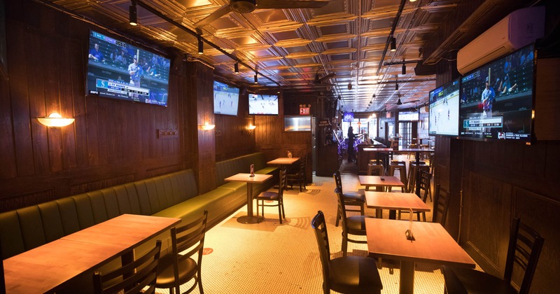 Interior, upholstered seating by a wall  with tables and chairs, lined up tables for two, TVs