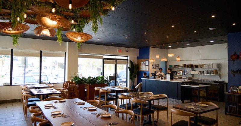 Interior, set wooden tables, hanging lamps and greenery add a welcoming touch