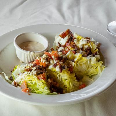 Wedge salad topped with crumbled bacon and diced tomato, served with bleu cheese dressing.