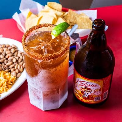 Michelada in a chilled, chili-rimmed glass beside a beer bottle.