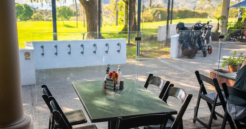 Outdoor cafe seating area with a green table, black chairs, and a view of a golf course
