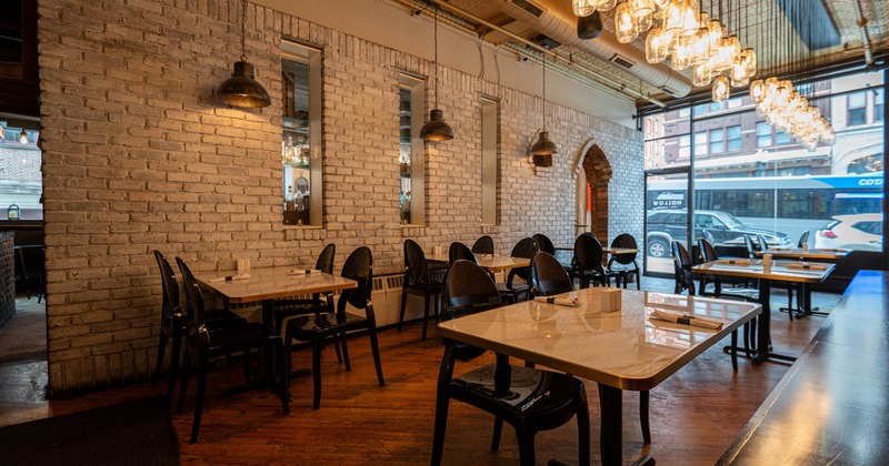 Restaurant interior with white brick walls, industrial lamps, marble tables, and large windows